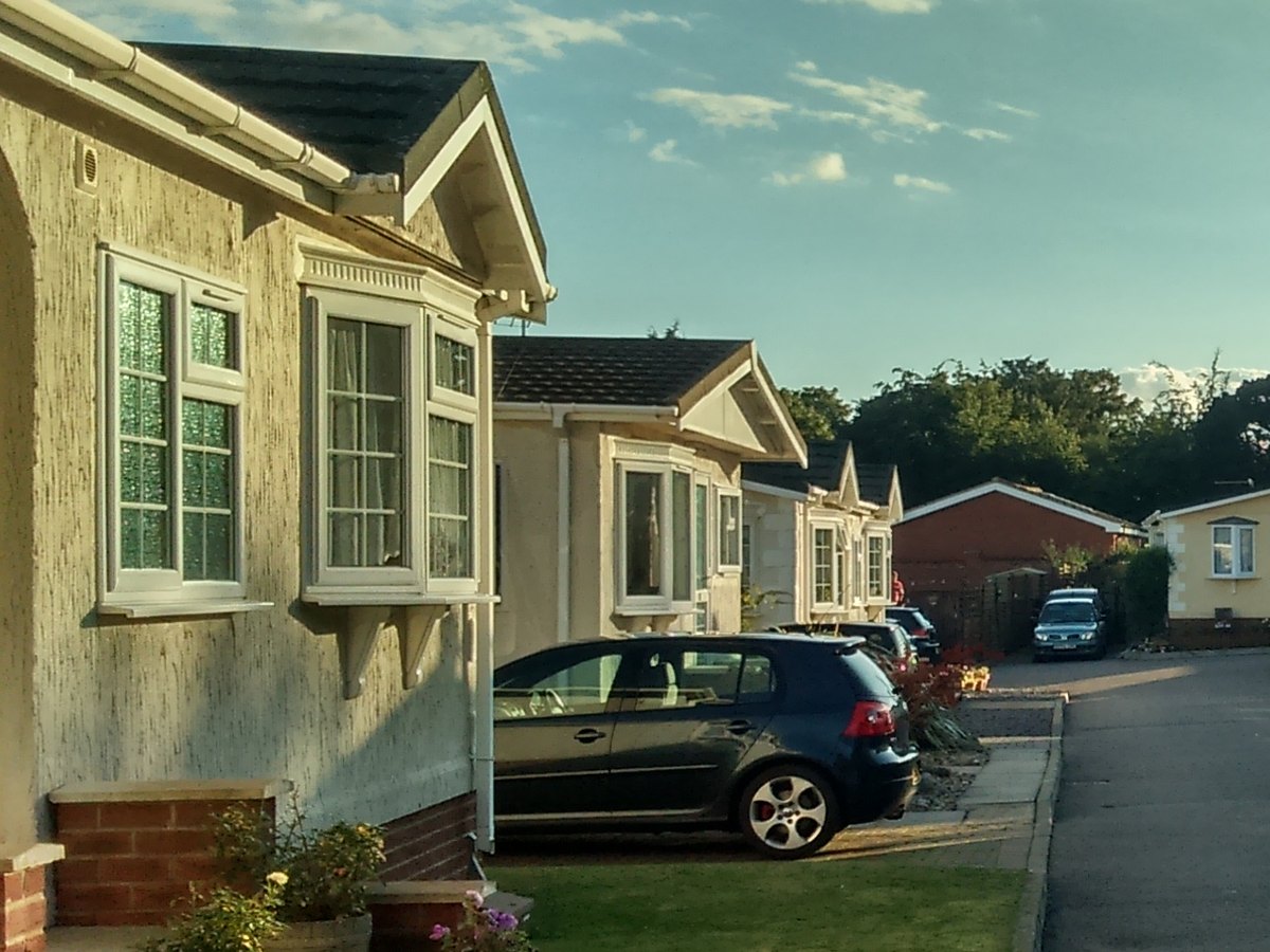 A row of park homes with bay windows and brick-edged flower beds