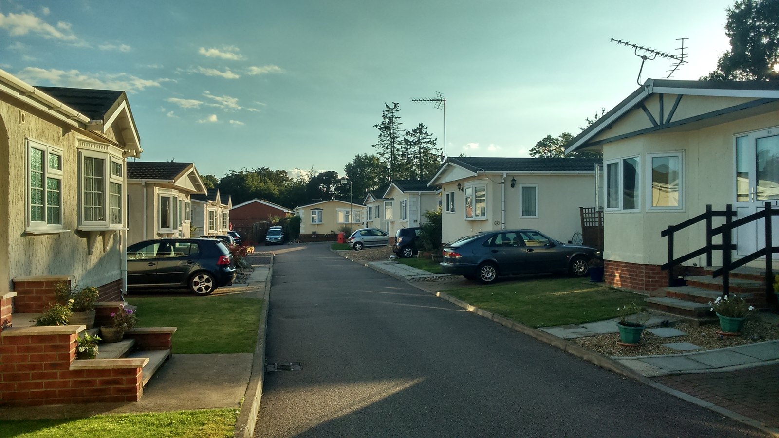 Park homes and lawns either side of the road through Woodlands Park on a summer evening